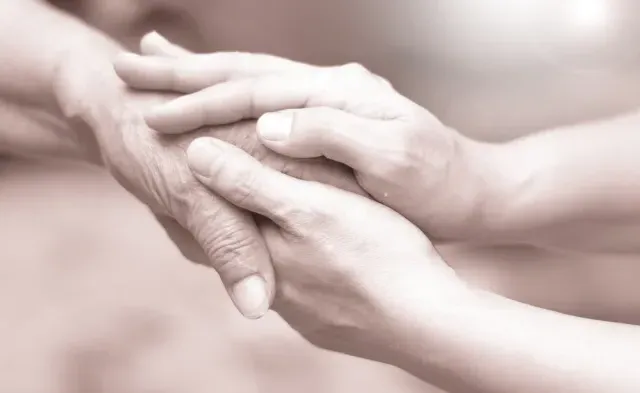 Caregiver, career hand holding elder hand in hospice care. 